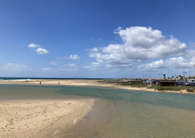 Estuario del Río Salado en Conil de la Frontera, con arena dorada, aguas tranquilas y cielo despejado.